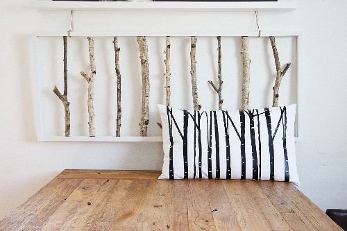 Scatter cushion with pattern of branches on wooden table below 3D artwork made from birch branches