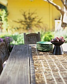 Wooden table in open air with a bowl of plums & pile of plates