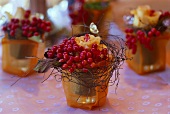 Tischgestecke mit Beeren und Rosen in tüllüberzogenen Gläsern