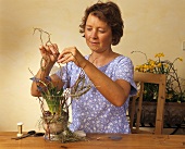 Frau dekoriert Glasvase mit Traubenhyazinthen und Zweigen