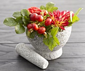 Rose hips and autumn flowers in stone mortar