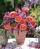 Arrangement of roses and lilac in terracotta vase, angel