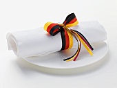 White fabric napkin with ribbon in colours of German flag