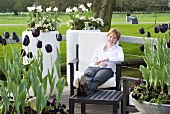 Frau auf Gartenstuhl zwischen Blumenschalen mit Tulpen