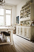 Küche mit antik weiss gestrichenem Holzschrank und feinen Polsterstühlen an einfachem Holztisch