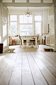Blick durch Flügeltür in Wohnküche mit antiken Stühlen am rustikalen, weiss gestrichenen Esstisch