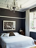Elegantes Schlafzimmer mit rauchblauen Wänden unter der weissen Stuckdecke mit Kronleuchter