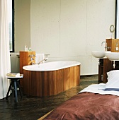 Das Bad im Schlafraum mit freistehender, holzverkleideter Badewanne und Holzsäule mit zwei Waschbecken