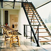 Einläufige Stahlholztreppe vor Fensterfront und hölzerne Armlehnstühle auf altem Dielenboden