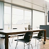 Moderner Esstisch auf Rollen und schwarze Stühle vor der Fensterfront im offenen Wohnraum