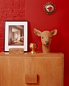 Deer's head sculpture and black and white photo on cabinet against bright red wall