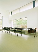 Minimalistischer Wohnraum - langer schwebender Esstisch mit Designer Stühlen und durchgehender Sitzbank vor Panoramafenster