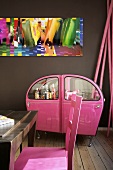 Wohnraum in Brauntönen mit schriller Getränkebar aus pinkfarbenen Autotüren unter knalliger Fotokunst