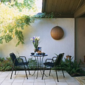 Terrace with round table and chairs in front of white wall