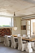 Dining room with long dining table, chairs with white loose covers and pendant lamp