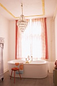 Free-standing bathtub in traditional bathroom with crystal chandelier and checked curtains