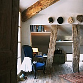 Rustic wooden beams in converted attic room with blue armchair and collection of hats on wall