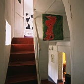 Stairwell with red staircase, white wooden balustrade and modern paintings on wall