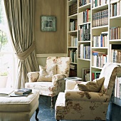 Bücherwand mit versetzten Regalen, Sesseln mit floralem Muster, gepolsteter Hocker und schweren Vorhängen in traditionellem Wohnzimmer