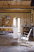 Geräumige Landhausküche mit Terrakottafliesen, einfacher, gemauerter Küchentheke und einem weissen Schaukelstuhl