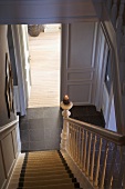 View down staircase with lit candle on newel post through open door into room with wooden floor