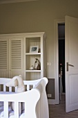 Weisser Kinderzimmerschrank mit Lamellentüren und Regalen; davor ein weisses Kinderbett mit Stoffhund