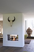 Fire in double sided fireplace below buffalo skull; head of Buddha in background
