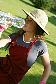 A young woman in a straw hat and gardening gloves drinking mineral water from a bottle