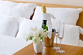 A bottle of champagne, glasses and a bunch of tulips on an occasional table in a hotel room