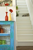 A blue cabinet next to a flight of white, wooden stairs