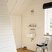 Waschbecken und Stuhl neben Fenster in einem weißen Holzhaus