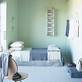 Ein Schlafzimmer mit Einzelbett , Bodenteppich und an der Wand aufgehängte Kleiderstücke
