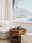 weiße Sessel und Rattantisch unter Fenster mit Meeresblick