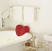 Ausschnitt einer freistehenden Badewanne unter Metallstange mit weißen Handtüchern und Kosmetikspiegel