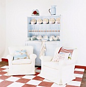 Zwei weiße Sessel vor blauen Wandschrank mit Geschirr