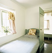 Einzelbett unter dem Fenster eines Schlafzimmers mit offener Tür zum Badezimmer