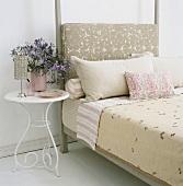 Ein Einzelbett mit gepolstertem Kopfteil und Metallnachttisch mit Blumenvase