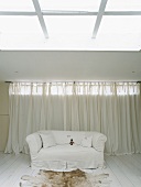 weiße Couch und Tierfell unter Deckenöffnung im schlichten Wohnbereich mit Dielenboden
