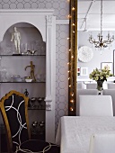 Tisch mit weißer Tischdecke vor großen Wandspiegel und Wandnische mit Glasregalen