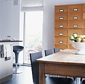 Vintage-Esstisch mit schwarzen Kunststoffstühlen, Schubladenschrank und raumhohem Fenster in moderner Küche