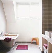 Badewanne mit Füssen in einem hellen Badezimmer mit gemauertem Waschtisch und grauem Fliesenboden