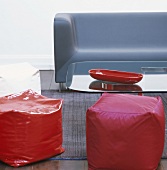 Rote Sitzhocker, blaue Couch und Glastisch mit roter Schale im Wohnzimmer
