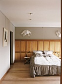 Schlafzimmer mit Doppelbett, einer Wandverkleidung aus Holz und darüberhängenden Kunstobjekten