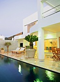 Loungers and exotic plants on terrace of house with swimming pool