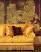Shimmering gold couch with scatter cushions and fringe in front of large, modern painting with wooden frame