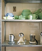 Crockery and other kitchen utensils on metal shelving against tiled wall