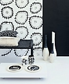 Still-life arrangement in black and white with bench, floor vases and patterned wallpaper