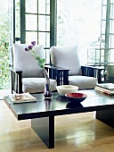 Zwei schwarze Sessel mit weißen Polster hinter Couchtisch mit Blumenvase und Schüsseln