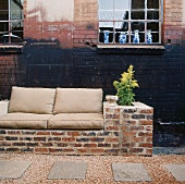 Eine gemauerte Couch mit sitzpolster vor Backsteinwand