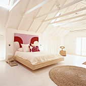 Ein Doppelbett mit buntem Kopfteil unter offener Dachbalkenkonstruktion